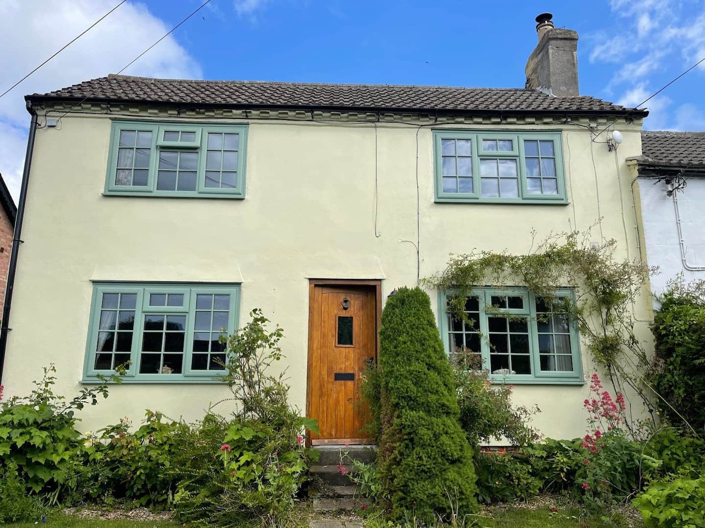 The front of Elm Cottage — an 18th-century stone cottage with cream render and sage-green window frames